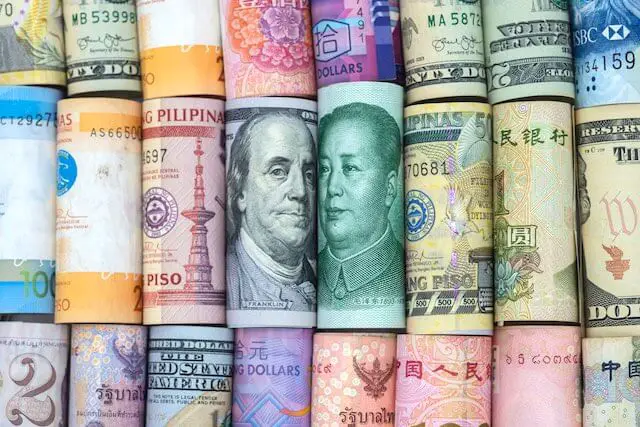 Rolled up currency bills in rows with a focus on the US dollar and Chinese yuan in the middle depicting global finance/international stocks