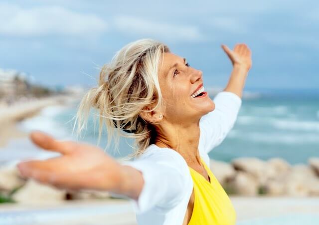 Happy retirement aged woman with arms outstretched as she looks up and embraces the day and beautiful weather