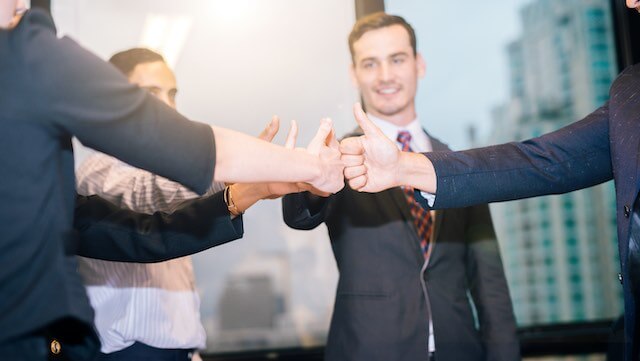 A group of four employees standing in a circle and giving a 'thumbs up' sign