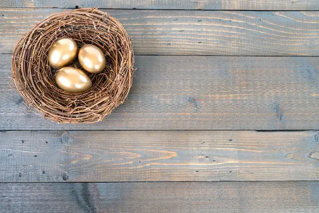 Golden retirement nest eggs in a straw basket sitting on a wooden surface