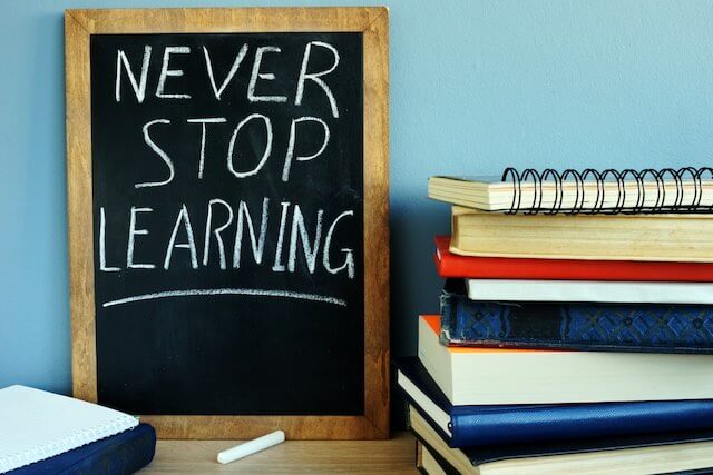 Words 'never stop learning' written on a small chalkboard leaned up against a wall on a desk next to a stack of school books