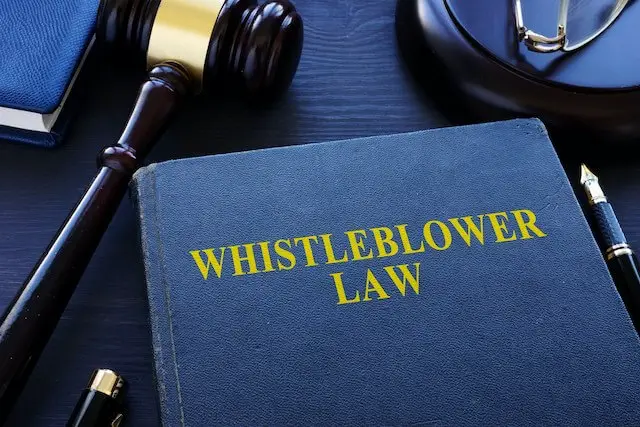 Book on a desk titled 'whistleblower law' next go a pen, glasses and judge's gavel