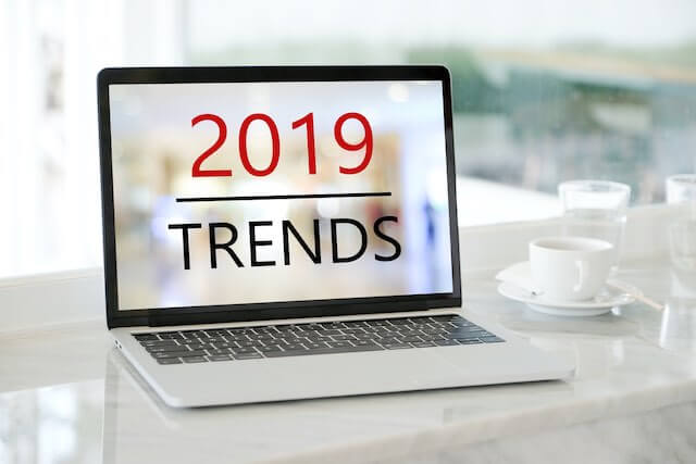 Laptop on a desk next to a coffee cup with the words '2019 trends' on the screen