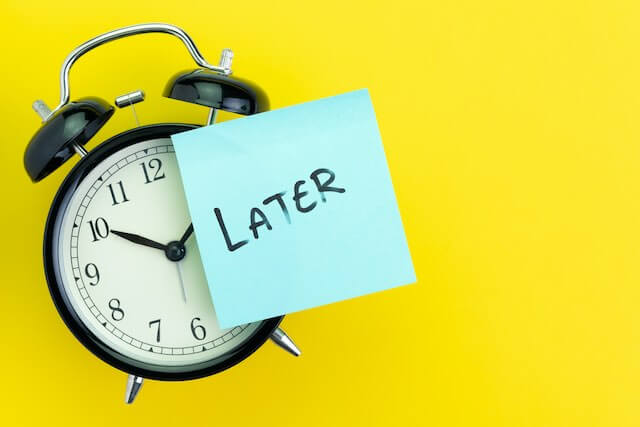 old style alarm clock with a sticky note on it that reads 'later' against a solid yellow background