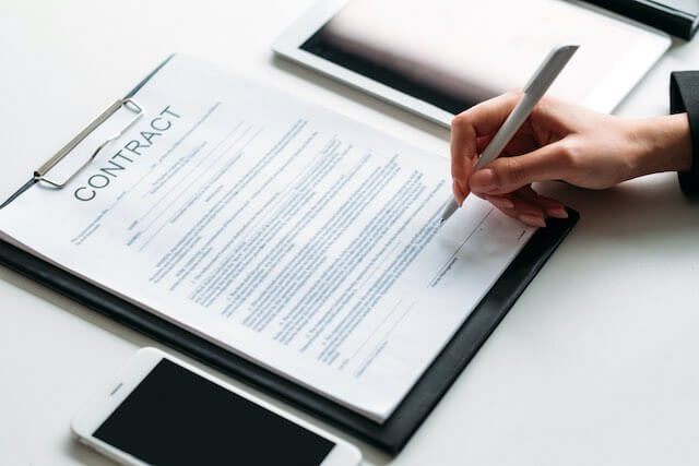 Contract on a desk with a close up of a person's hand holding a pen preparing to sign on the line at the bottom