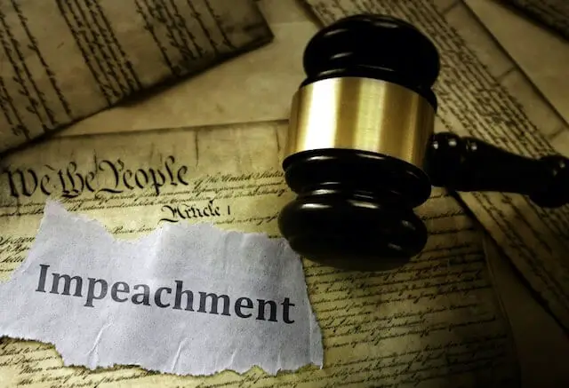 United States Constitution with a judge's gavel and a torn piece of paper with the word 'impeachment' written on it sitting on top of it