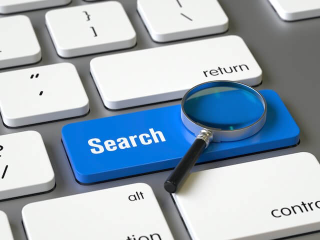 Close up of a blue button on a computer keyboard labeled 'search' with a magnifying glass sitting on top of it