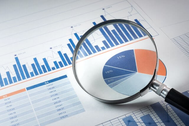 Magnifying glass focusing on a pie chart over a sheet of paper with various financial graphs and charts on it