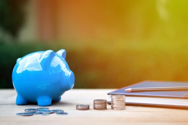 Blue piggy bank next to coins and a notepad on a desk