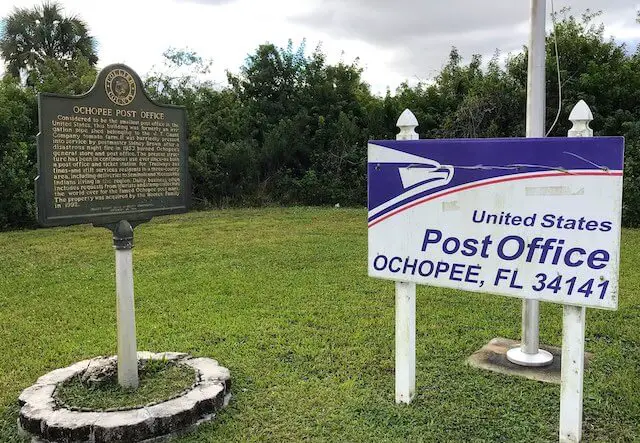 Historical landmark sign for the smallest Post Office in the country in Ochopee, FL next to a sign that reads 'United States Post Office Ochopee, FL 34141'