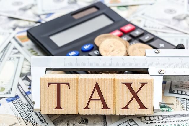 wooden block letters that spell the word 'tax' pictured on top of a spread of cash with a calculator in the background