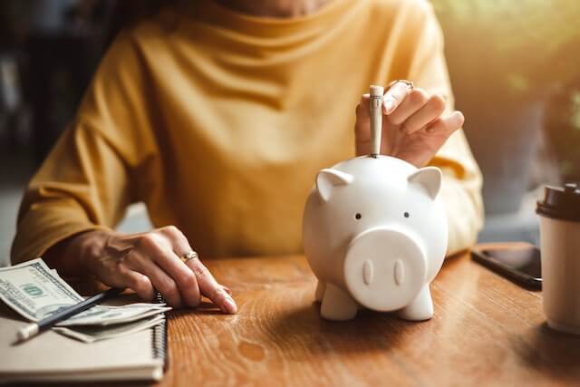 Woman sitting at a desk putting money into a white piggy bank