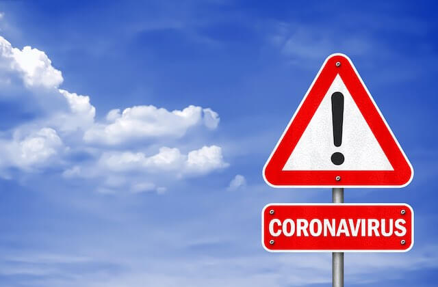Red and white road warning sign that reads 'coronavirus' pictured against a blue sky
