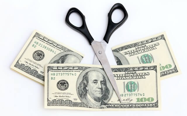 Scissors cutting two $100 bills in half against a solid white background