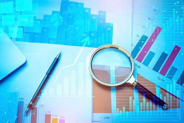 Series of financial charts spread out on a desk with a magnifying glass and pen sitting on top of them with a bar graph with a rising trend line overlaid on top of the image