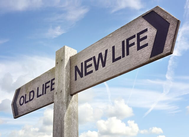 Directional sign against a blue sky that says "old life" on one side pointing in one direction and "new life" on the other side pointing in the opposite direction