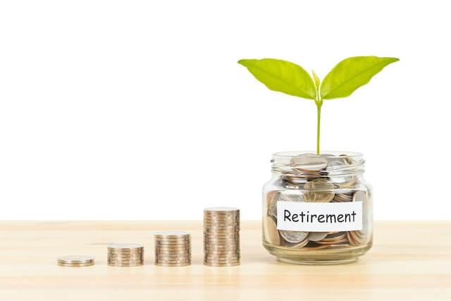 Four stacks of coins growing in size from left to right pictured next to a glass jar full of coins labeled 'retirement' with a green plant seedling growing out of it