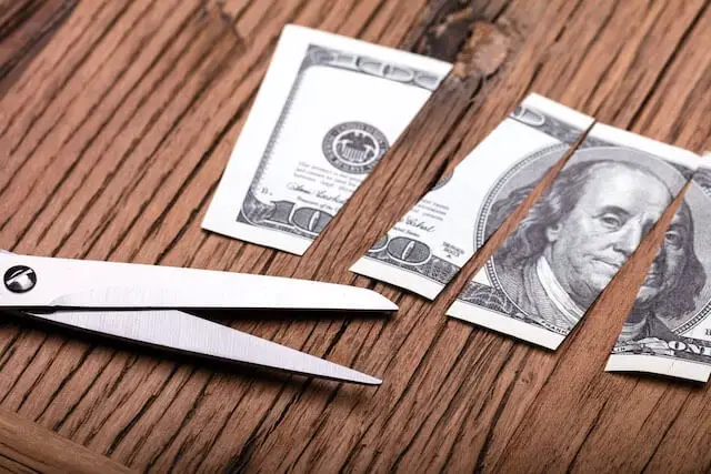 Scissors lying next to a $5 bill that has been cut into pieces on a wooden surface