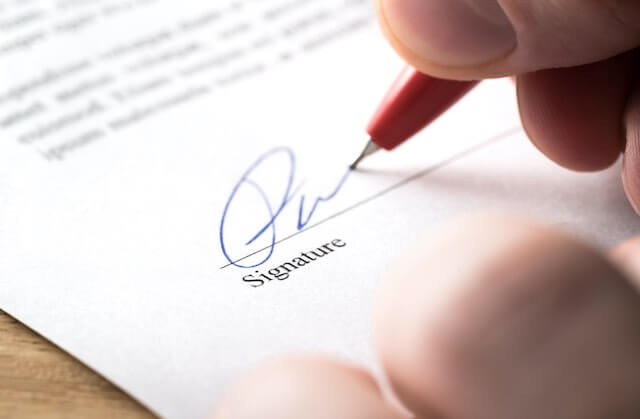 Close up of a person's hand signing the signature line on a contract