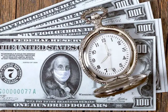 Spread of four $100 bills with a surgical mask pictured over the mouth and nose of Benjamin Franklin's photo on the top bill; a pocket watch is sitting on top of the bills to the right side