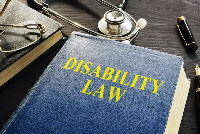 Book sitting on a desk with the words 'disability law' on it next to glasses, a pen and stethoscope