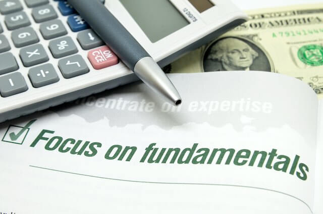 Booklet open to a page that reads 'focus on fundamentals' next to a box with a checkmark in it; a pen, calculator and cash are seen sitting just above the booklet