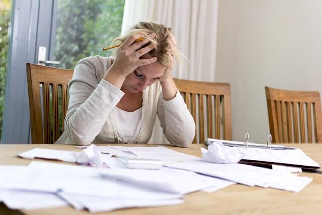 Middle aged woman with her hands on her head as she looks down at a spread of paperwork in frustration/stress/worry over debt/bills