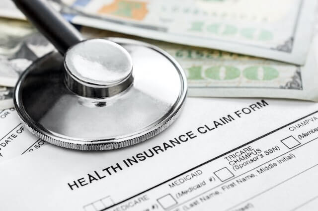 Close up of the top of a document labeled 'health insurance claim form' with a stethoscope and some cash lying on top of it