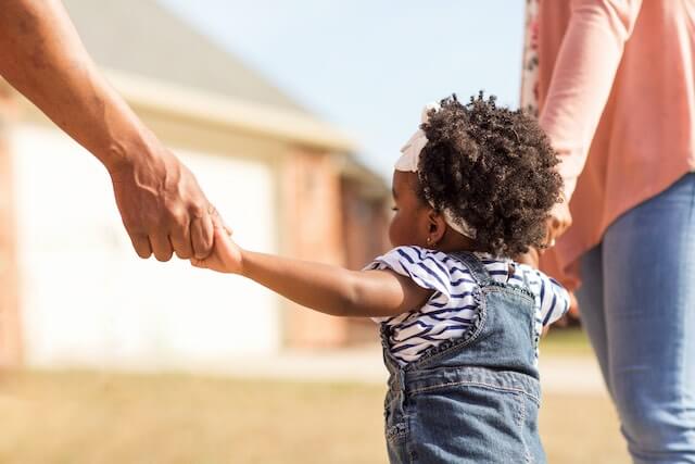 Little girl holding the hands of her parents as she walks