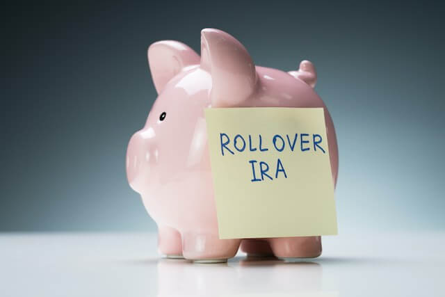 Pink piggy bank with a yellow post it note stuck to the side that reads 'Rollover IRA'
