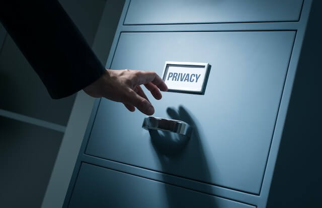 Close up of a man's hand reaching for a file cabinet labeled 'privacy' in a dark room