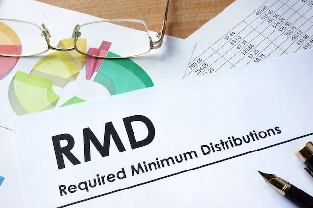 Sheet of paper on a desk that is labeled 'RMD Required Minimum Distributions' with a pen on top of it and sitting next to glasses and a spreadsheet