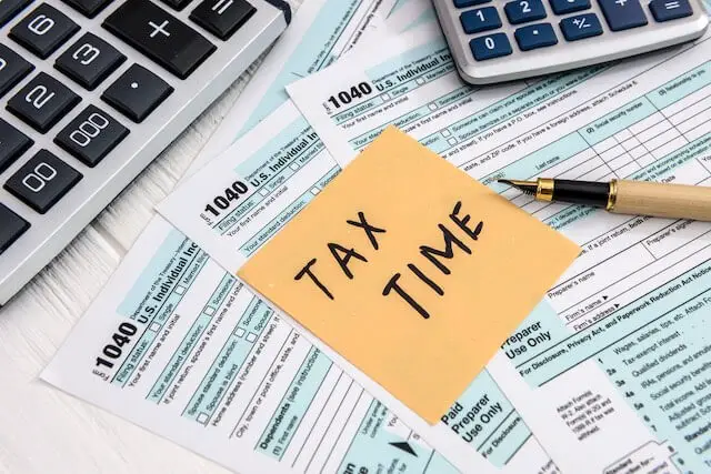 1040 tax forms spread on a desk with a pen, calculators and a post it note on top of them that reads 'tax time'