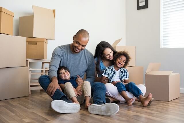 Young family (husband, wife and two young children) pictured sitting on the floor of their new home surrounded by moving boxes