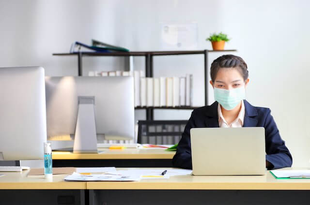 Businesswoman wearing a surgical face mask sitting at her desk in an office environment working on a computer