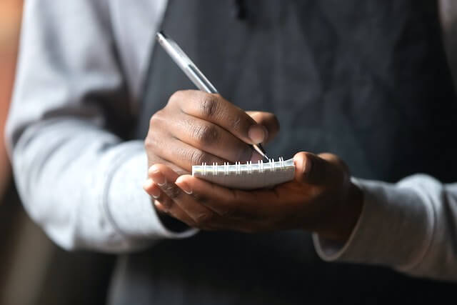 Close up of a woman's hands holding a small notepad and pen as she takes notes while standing