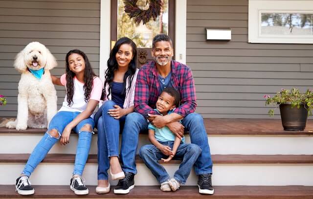 A family of four (parents in 30s or 40s, a young son and a teenage daughter and the family dog) sitting on the front porch of their house