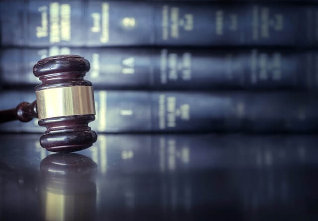 Judge's gavel on a wooden surface with a stack of law books seen blurred in the background behind it