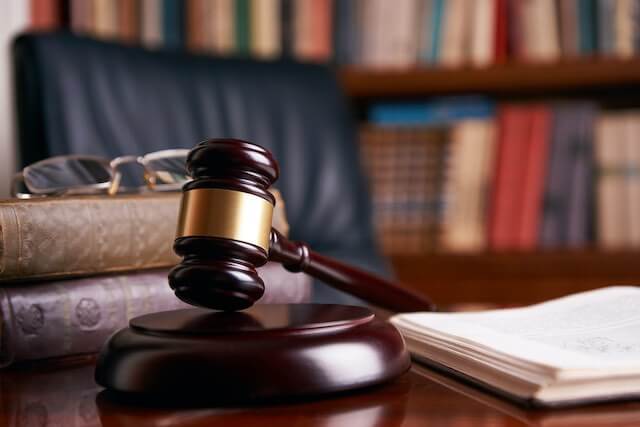 Wooden judge's gavel on a desk next to an open book and a stack of law books with glasses on top of them