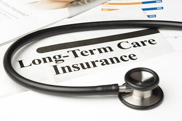 Words 'long-term care insurance' written on a piece of paper sitting on a desk next to a stethoscope