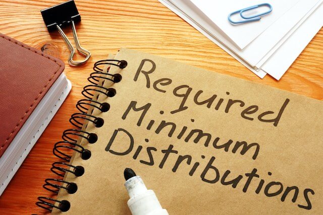 Notebook on a desk with the words 'required minimum distributions' written on the cover in black marker with the market sitting on top of it