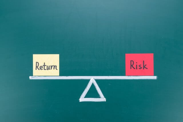 Balance scale in a level (flat) position with a box labeled 'return' on one side and a box labeled 'risk' on the other side