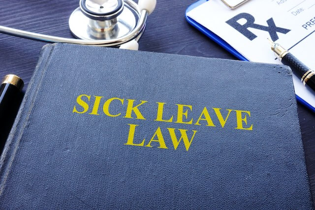 Book on a desk titled 'sick leave law' next to a stethoscope and prescription pad