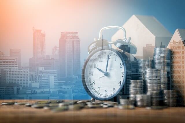 Old style alarm clock and stacks of coins pictured in front of a city skyline