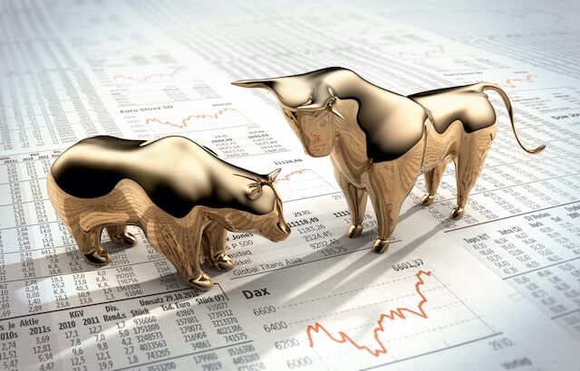 Golden colored bear and bull figurines pictured on top of financial listings from a newspaper