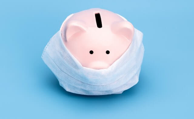 Pink piggy bank wearing a surgical face mask pictured against a solid blue background