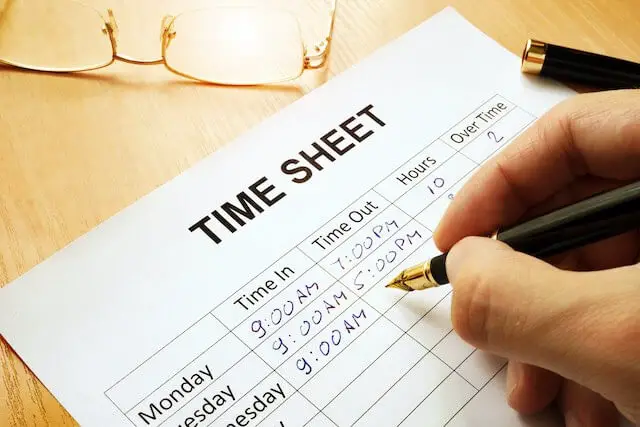 Close up of a person's hand filling out work times on a piece of paper labeled 'time sheet'