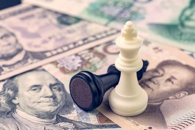 A black and a white chess pawn sit on top of spread of US dollars and a Chinese Yuan international currency