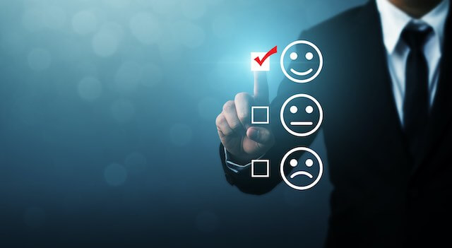 Businessman tapping a touchscreen on a positive feedback rating indicated by a smiley face emoji; two other options appear underneath of a neutral face emoji and a frowning face emoji