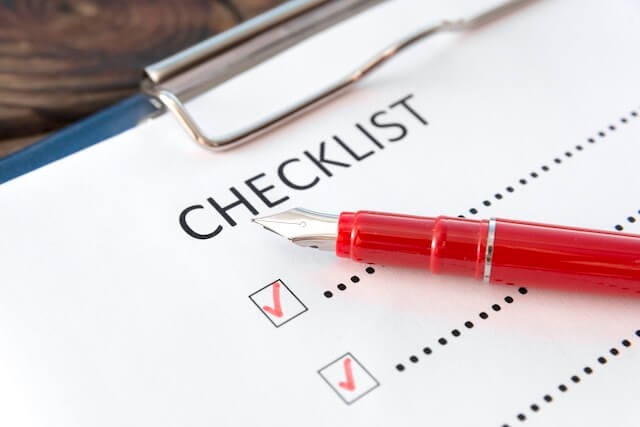 'checklist' written at the top of a sheet of paper with a red pen on top and two boxes on the list marked with red checkmarks